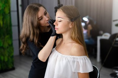 Beyaz tenli genç bir kız kaş modelini düzeltiyor.