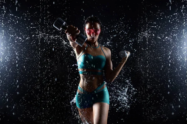 Krásná mladá dívka v sportovní představuje s činkami v aqua studio. Kapky vody šíří o její vhodnosti tělo. Dokonalá postava na pozadí postříkání vodou — Stock fotografie