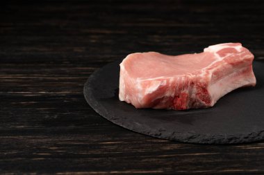 Siyah bir taş kesme tahtası üzerinde bir adet çiğ domuz pirzolası biftek üst görünümü. Ahşap masa.