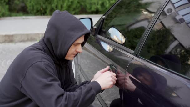 Zloděj aut ukrást auto lámání dveří kriminální práce lupič únosy auto zloděj černý balaclava mikina se snaží vloupat do vozidla šroubovák Street zločin násilí gangster lupič automobil — Stock video