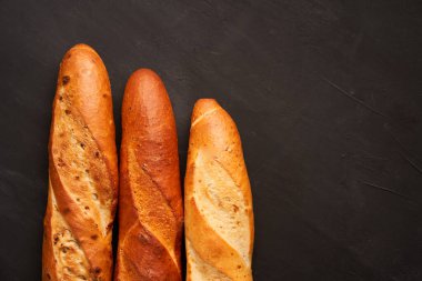 Üç çıtır Fransız ekmeği koyu siyah masa arkaplanı susam tohumları üzerine uzanır. Klasik Fransız ulusal pastaları. Menü veya reklam için alanı kopyalayın.