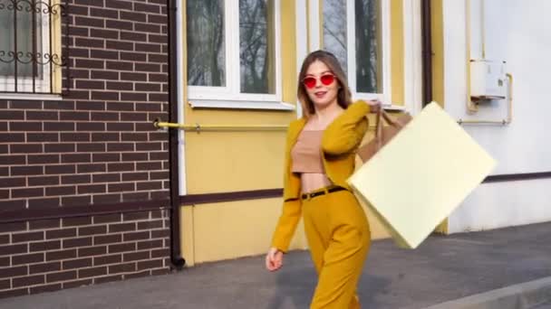 Ein junges kaukasisches europäisches Mädchen Shopaholic läuft mit Einkäufen in Paketen über die Straße. — Stockvideo