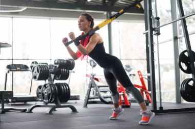 Spor salonundaki süspansiyon sistemiyle egzersiz yapan atlet kadın. Güzel beyaz kadın özel kayışla esneme kuvveti egzersizi yapıyor. Orta yaşlı kız egzersizi. 