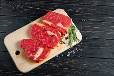 Siyah tahta bir arka planda, kesme tahtasına biberiyeli üç parça sulu çiğ biftek. Biber ve tuz çeşnili barbekü ya da ızgara et.