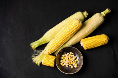 Yeşil yaprakları ile mısır koçan masada yatıyor. siyah renk arka plan. Metin için alan kopyalama.