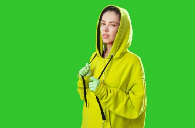 Güzel beyaz kadın, limon rengi kapüşonluyla stüdyoda yeşil arka planda.