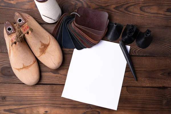 ノートのための紙の空の白いシートと暗い木製のテーブルの上に靴と木製の靴のための革サンプル デザイナー家具の服 靴屋のワークスペース — ストック写真