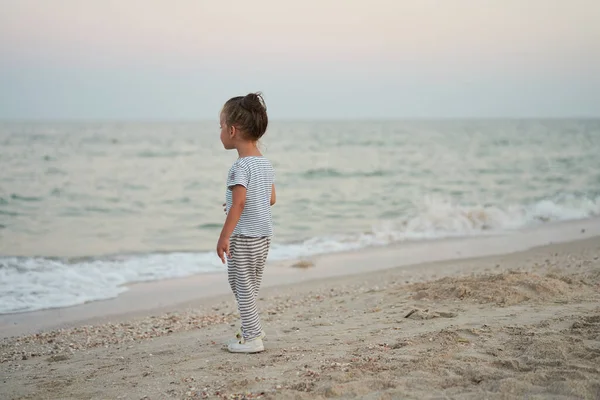 子供遊び砂のビーチ小さな女の子遊び悲しいだけ夏休み白人女性3歳服を着たデニム近く海の水 — ストック写真