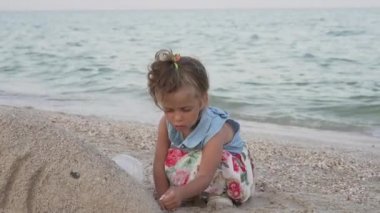 Kum plajı oynayan küçük kız yaz tatilinde yalnız başına üzgün oynuyor.