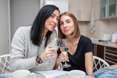 Modern tarz mutfakta şarap ve pastayla tanışan arkadaşlar. Genç kadınlar ellerinde şarap kadehleriyle gülüp şakalaşıyorlar. İki kız ev mutfağında şarap içiyor..