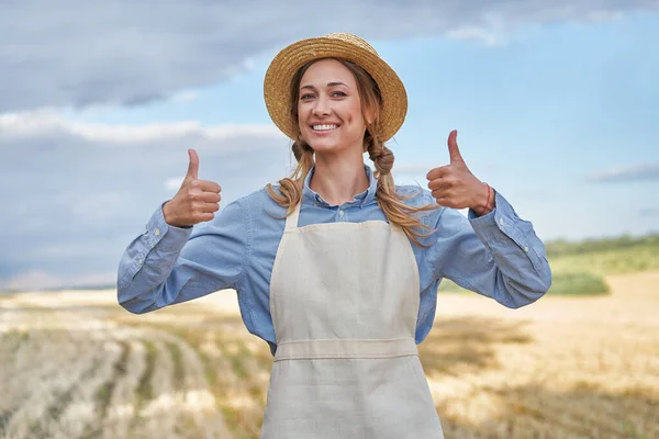 女性農家わら帽子エプロン立っ農地笑みを浮かべて親指を示すサイン女性農業専門家農業ビジネス幸せな正の原因アジアの労働者農業分野 — ストック写真
