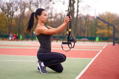 Trx spor sahası kullanan kız sporcu eğitimi. Karışık ırk genç yetişkin kadın spor süspansiyon sistemi. Açık havada esnemek için sağlıklı bir yaşam tarzı. Vücut makineni yap                            