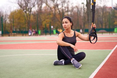 Trx spor sahası kullanan kız sporcu eğitimi. Karışık ırk genç yetişkin kadın spor süspansiyon sistemi. Açık havada esnemek için sağlıklı bir yaşam tarzı. Vücut makineni yap                            
