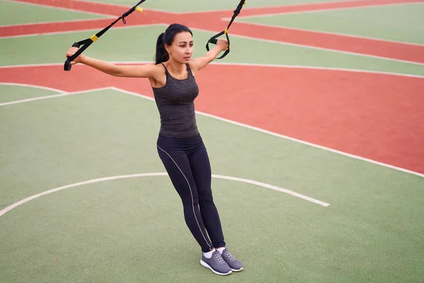 Trx spor sahası kullanan kız sporcu eğitimi. Karışık ırk genç yetişkin kadın spor süspansiyon sistemi. Açık havada esnemek için sağlıklı bir yaşam tarzı. Vücut makineni yap                            