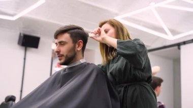 Berber dükkanında oturan yakışıklı mavi gözlü adam. Kuaför kadın onun saçını kesiyor. Kadın berber.. 