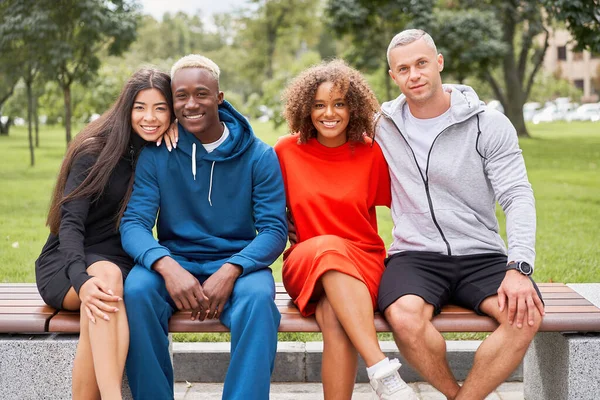 多民族グループ10代の友人 アフリカ系アメリカ人アジア人の学生が一緒に時間を過ごす多人種間の友情幸せな笑顔人々がカラフルなスポーツウェアを着てベンチパーク屋外 — ストック写真