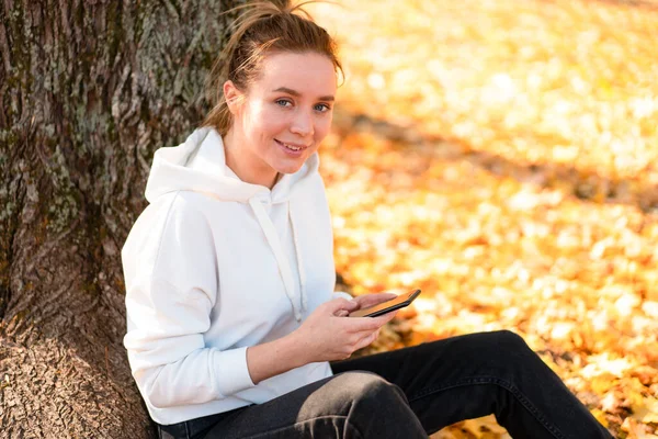 Woman White Hoodie Sweater Hood Sits Ground Park Holding Cellphone — Stock Photo, Image