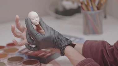 Artist fitting eyes into doll head focusing on fine details and precision needed to create realistic facial features, demonstrating expert craftsmanship in doll making at workshop