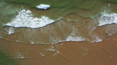 Aerial drone view of sea waves gently crashing on sandy beach leaving trail of foam on shore. The natural beauty of ocean and coast creates serene and peaceful beach scene