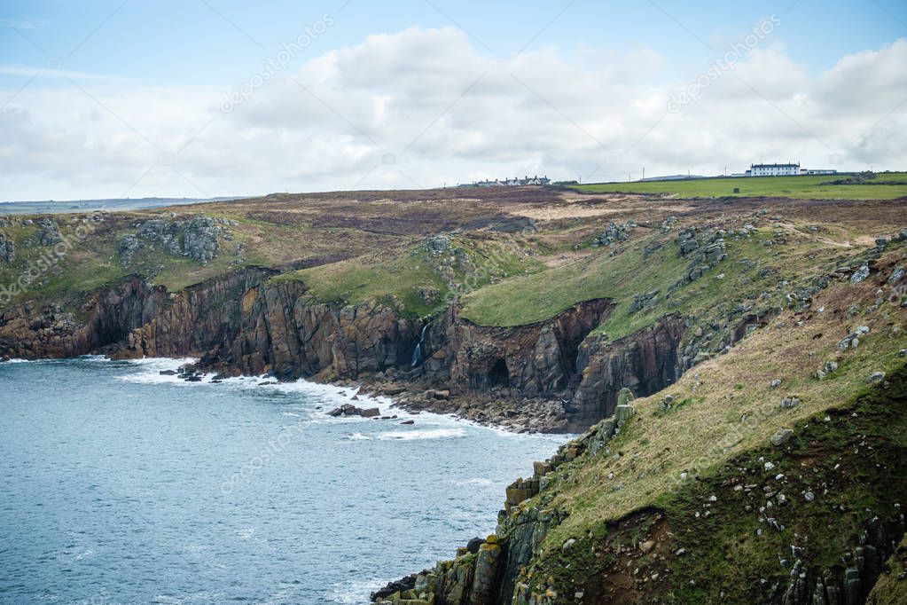 the coastline is made up of steep, high shores, overgrown with green grass; There are white waves along the rocks along the coast