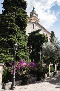 boş sokak ve fenerler çit önce; büyük iğne yapraklı ağaçlar ve onların arkasında bir kule ile bir bina