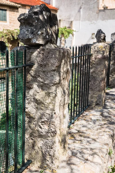 a yard around the house with concrete posts with stones at the ends; black metal fence between posts; one pillar is highlighted with sharpness