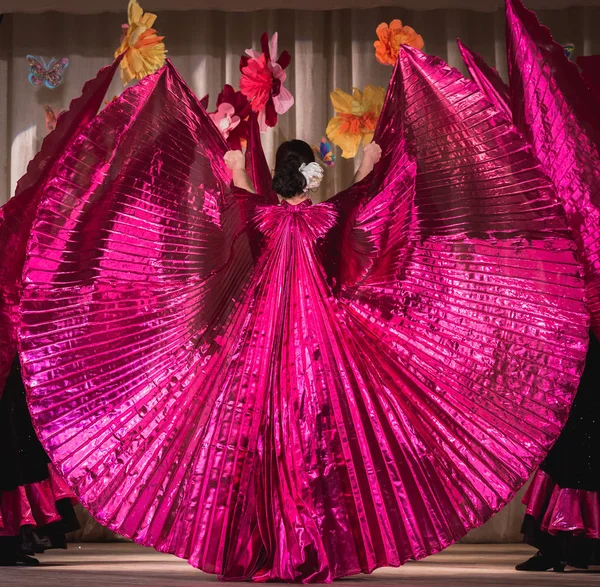 oriental dance on stage in bright colors in purple tones with wide wings for fans; view from the back to the dancers