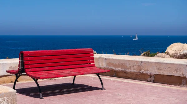 view of the sea and yacht, the horizon where blue waters blend with the sky, the red bench for holidaymakers is in the foreground