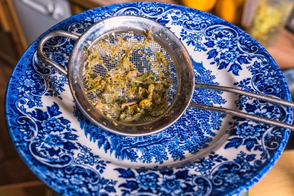 white plate with blue ornaments and a strainer with linden blossom tea flowers and stems on it