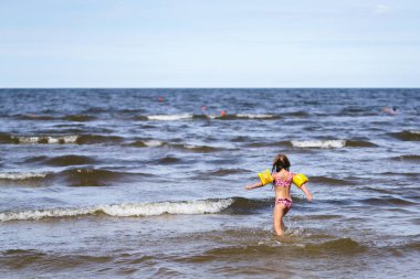 Yazın küçük beyaz dalgalarla deniz manzarası, yüzmek için koşan küçük bir kız..