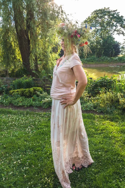 one woman with a summer solstice wreath on her head, standing in the garden on a pose