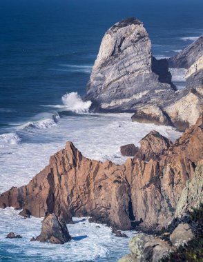 Atlantik kıyısının kayalara vuran renkli kayalıkları ve beyaz dalgaları; yüksek kıyıdan aşağıya bakan.