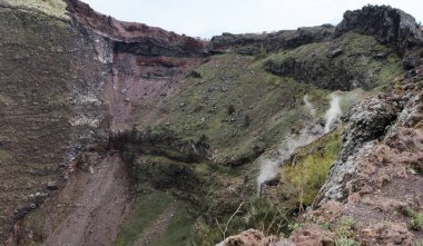 Naples, Italy - 04.28.2025: The crater wall of Mount Vesuvius on the opposite side from the first viewpoint. On the right side, steam is visible from the depths of the earth.