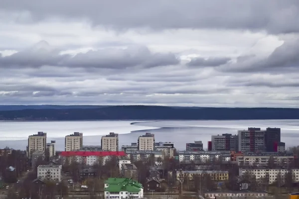 Vista de la ciudad y el lago desde un punto alto. Dramáticas nubes oscuras sobre medio lago cubierto de hielo . — Foto de Stock