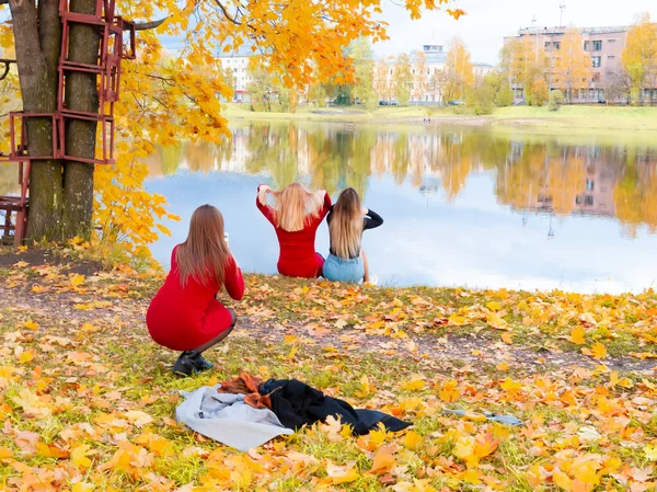 Две девушки сидят на берегу реки, и третья девушка фотографирует их . — стоковое фото