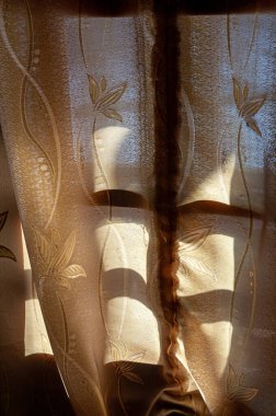 Parlak güneş ışığını yansıtan bir perdeyle çevrili küçük bir pencere.