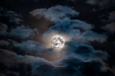 Gece gökyüzü bulutların arasında parlak bir dolunay ile