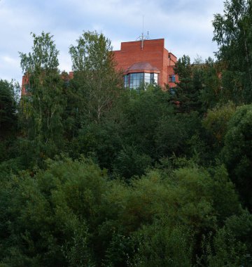 Ağaçların arasından süzülen kırmızı tuğlalı bir binanın tepesindeki manzara.