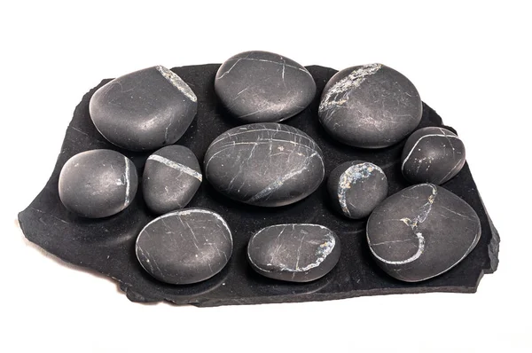 Shungite levhasının üzerine beyaz bir arka planda izole edilmiş birkaç shungite taşı bırakılmış.