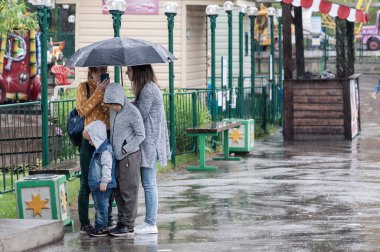Petrozavodsk, Rusya - 1 Ağustos 2020 Eğlence parkında sağanak yağmurdan saklanan gençler ve çocuklar