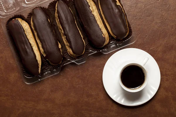 siyah kahve, çikolata Eclair, beyaz bir fincan kahve, beyaz tabak, kahverengi bir masada, bir stand üzerinde dört eclairs