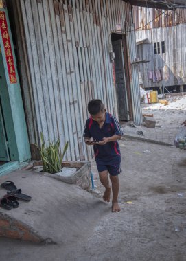Sihanoukville, Kamboçya. 25 Şubat 2019 : Sihanoukville balıkçı Köyü'ndeki ahşap evine dönerken el telefonuyla oynayan bir çocuğun sahnesi.