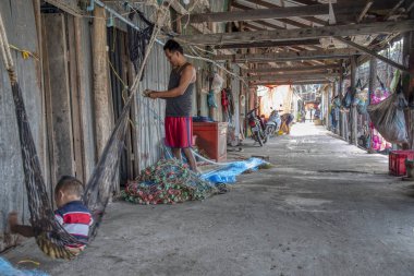 Sihanoukville, Kamboçya. 26 Şubat 2019: Sihanoukville Balıkçı Köyü'ndeki ahşap evinin önünde balıkçıağı tamir eden balıkçının sahnesi. 