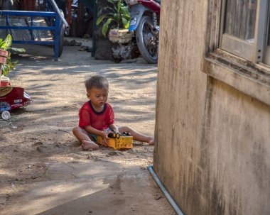 Sihanoukville, Kamboçya. 25 Şubat 2019 : Sihanoukville balıkçı Köyü'ndeki evinin yanındaki kumda tek başına oynayan küçük çocuk sahnesi.
