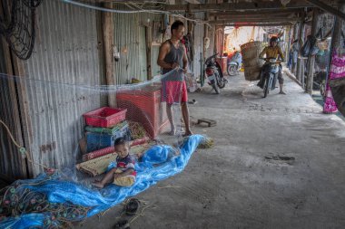Sihanoukville, Kamboçya. 26 Şubat 2019: Sihanoukville Balıkçı Köyü'ndeki ahşap evinin önünde balıkçıağı tamir eden balıkçının sahnesi. 