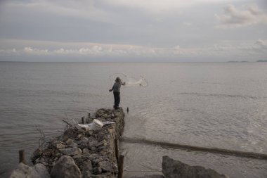 Perak, Malezya.7 Mayıs 2019: Tanjung Sepah plajında karides yakalamaya çalışan yüksek gelgit sırasında deniz kenarında duran Malay adam denize ağ dökme, Lekir.