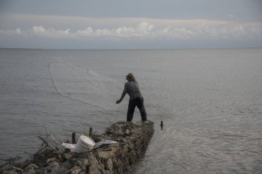 Perak, Malezya.7 Mayıs 2019: Tanjung Sepah plajında karides yakalamaya çalışan yüksek gelgit sırasında deniz kenarında duran Malay adam denize ağ dökme, Lekir.