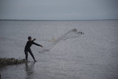 Perak, Malezya.7 Mayıs 2019: Tanjung Sepah plajında karides yakalamaya çalışan yüksek gelgit sırasında deniz kenarında duran Malay adam denize ağ dökme, Lekir.