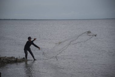 Perak, Malezya.7 Mayıs 2019: Tanjung Sepah plajında karides yakalamaya çalışan yüksek gelgit sırasında deniz kenarında duran Malay adam denize ağ dökme, Lekir.