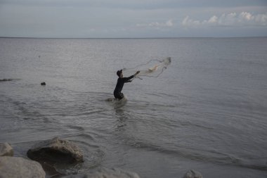 Perak, Malezya.7 Mayıs 2019: Tanjung Sepah plajında karides yakalamaya çalışan yüksek gelgit sırasında deniz kenarında duran Malay adam denize ağ dökme, Lekir.